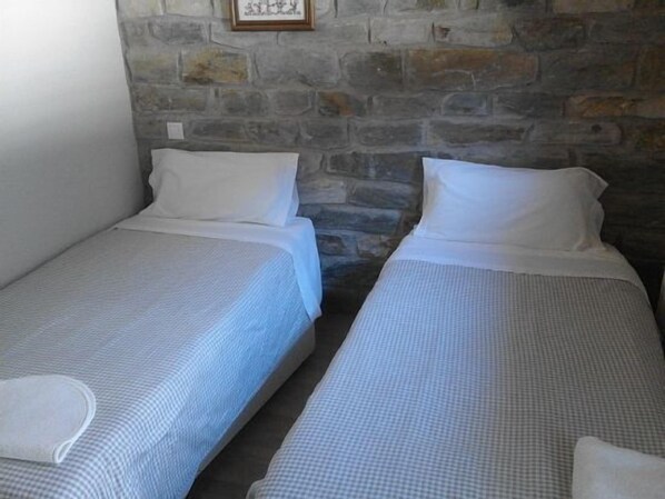 Two single beds with white linens in a room with a stone wall.