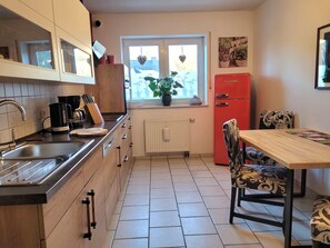 A modern kitchen with a sink, stove, and refrigerator. There is a window with a view of the outside, and a dining table with chairs.