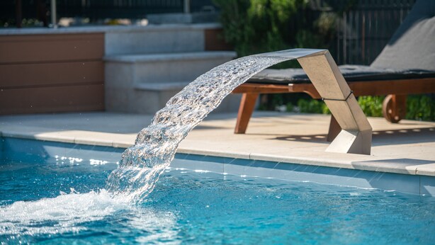 Una piscina con fuente, una silla de descanso y una repisa de hormigón.