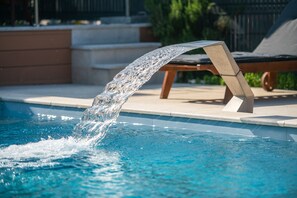 A pool with a water feature, a lounge chair, and a concrete ledge. - Large heated pool, sauna, jacuzzi, charging station for electric vehicles 22kW (Musalez)