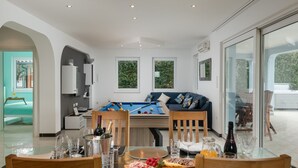 Una sala de estar moderna con una mesa de billar, un sofá con cojines y un comedor con una mesa dispuesta para dos personas.