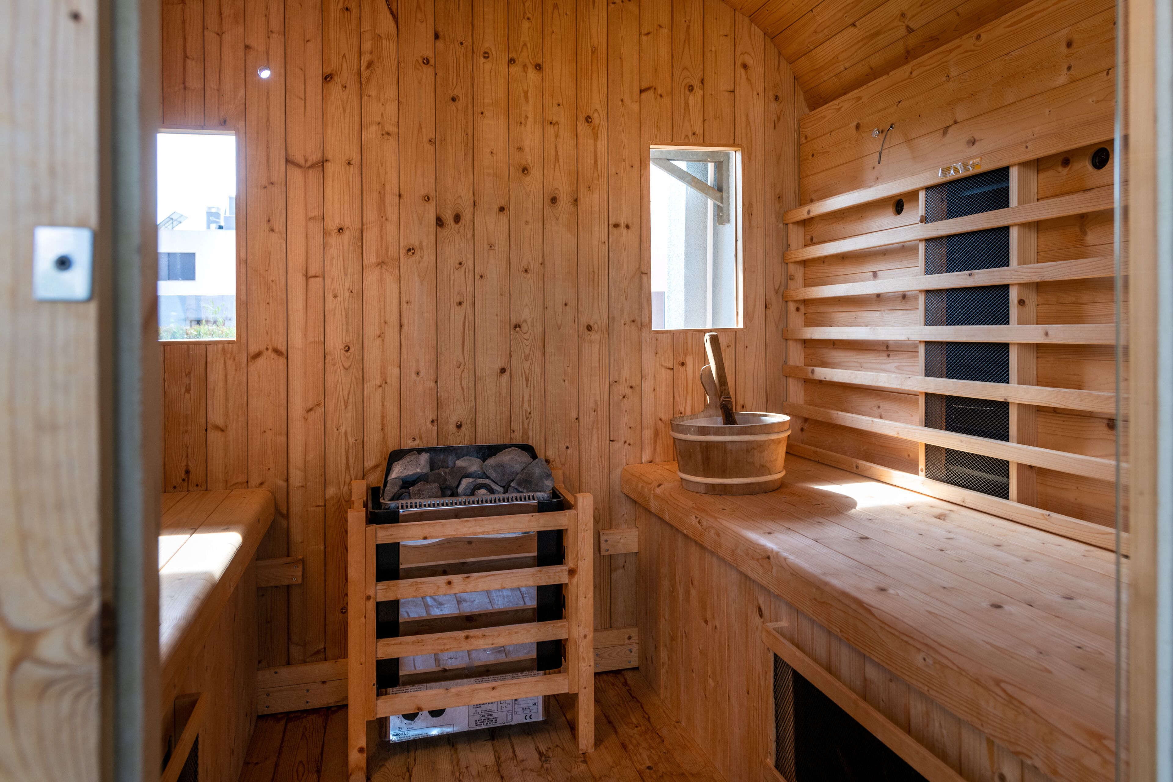 A wooden sauna room with a bench, a bucket, and a window.