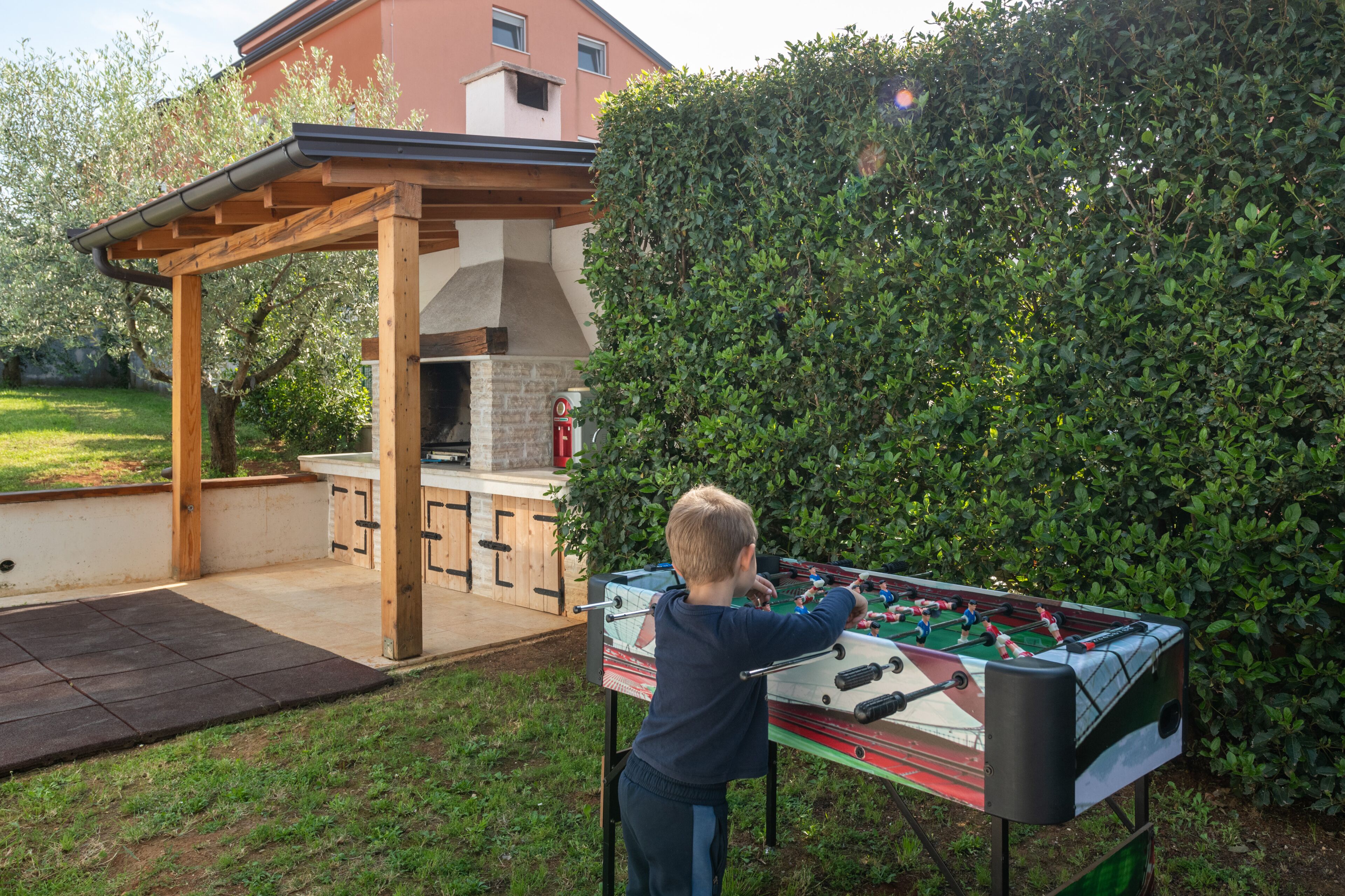 Una pergola de fusta amb zona de barbacoa, taula de futbolí i forn de rajola.
