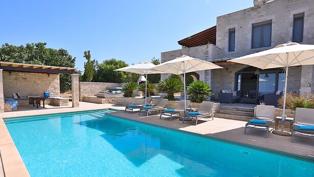 Ein Pool mit Liegestühlen und Sonnenschirmen, umgeben von Steinmauern und Pflanzen.