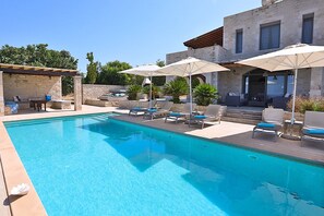 A swimming pool with lounge chairs and umbrellas, surrounded by stone walls and vegetation. - Villa Athene-modern stone villa with sea views, close to the beach, heated pool (Rethymno)