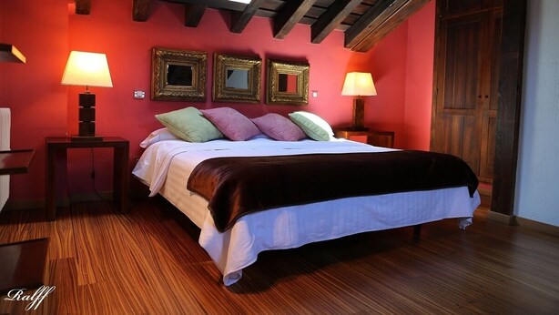 Une chambre avec un plafond en bois, un lit recouvert de linge de lit blanc et agrémenté de plusieurs oreillers, deux lampes de chevet et trois miroirs encadrés accrochés au mur.