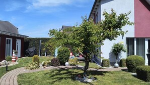 Ein Wohngebäude mit einem gepflegten Garten, einschließlich Rasenflächen, Hecken und einem Baum.