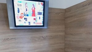 A small room with a white table and two stools, a TV mounted on the wall displaying a shopping channel, and a wooden panel wall. - Smart Apartment Krehivska 7 (Lviv)