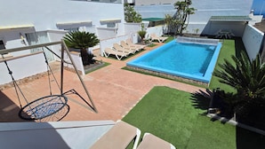 Una piscina en la azotea con un columpio, sillones de descanso y césped artificial.