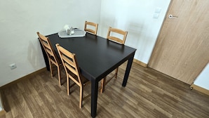 Un comedor con una mesa negra, cuatro sillas de madera y una bandeja pequeña con salsas y aderezos.