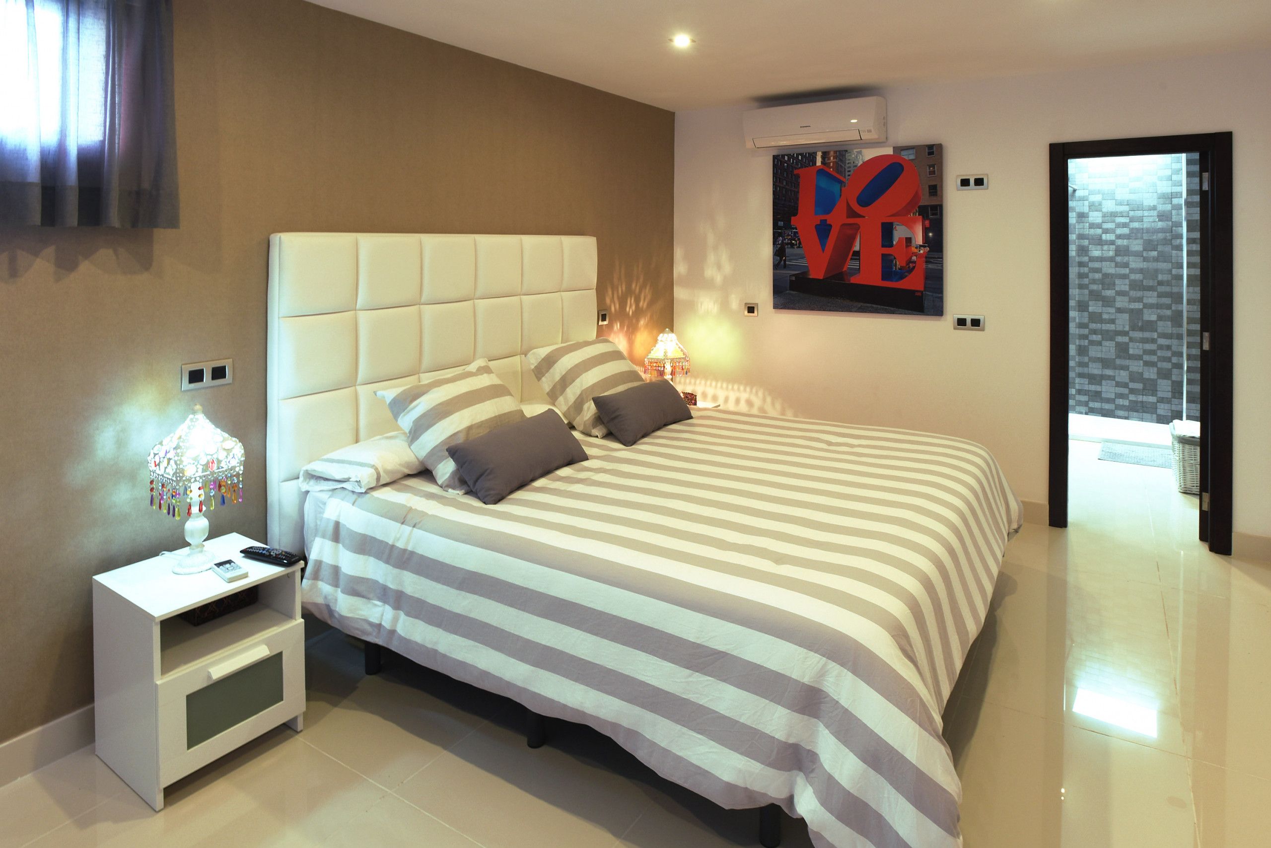 A modern bedroom with a large bed, a nightstand with a lamp, and a painting on the wall.