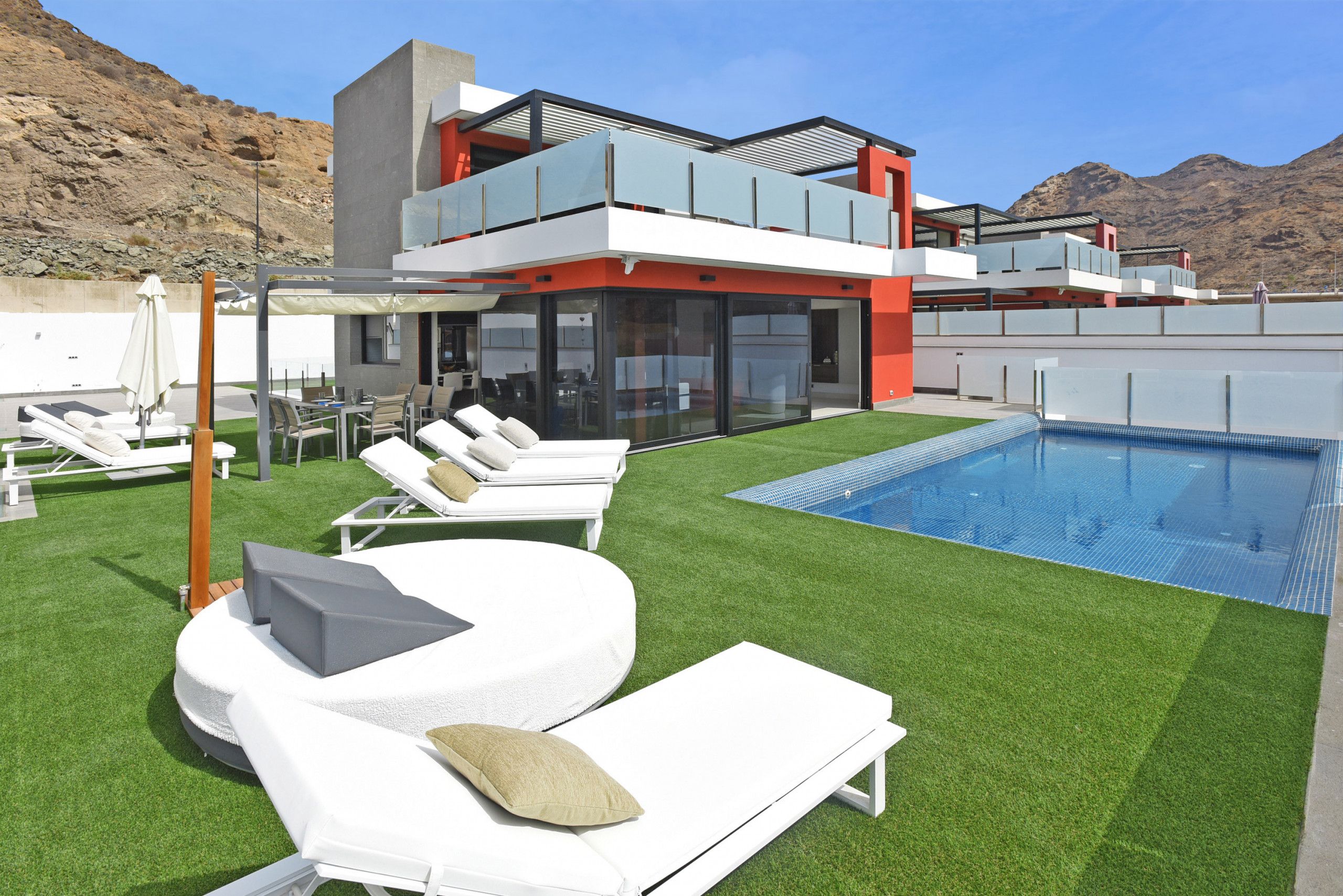 Un espace piscine extérieur moderne, doté d’une pelouse artificielle, de chaises longues blanches et d’une piscine à l’eau d’un bleu limpide.