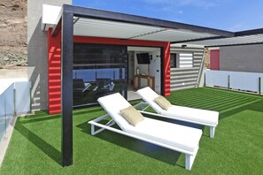 A modern outdoor lounge area with two white sunbeds and a glass door leading to an interior space. - Villa Morro del Guincho 29 (Mogán)