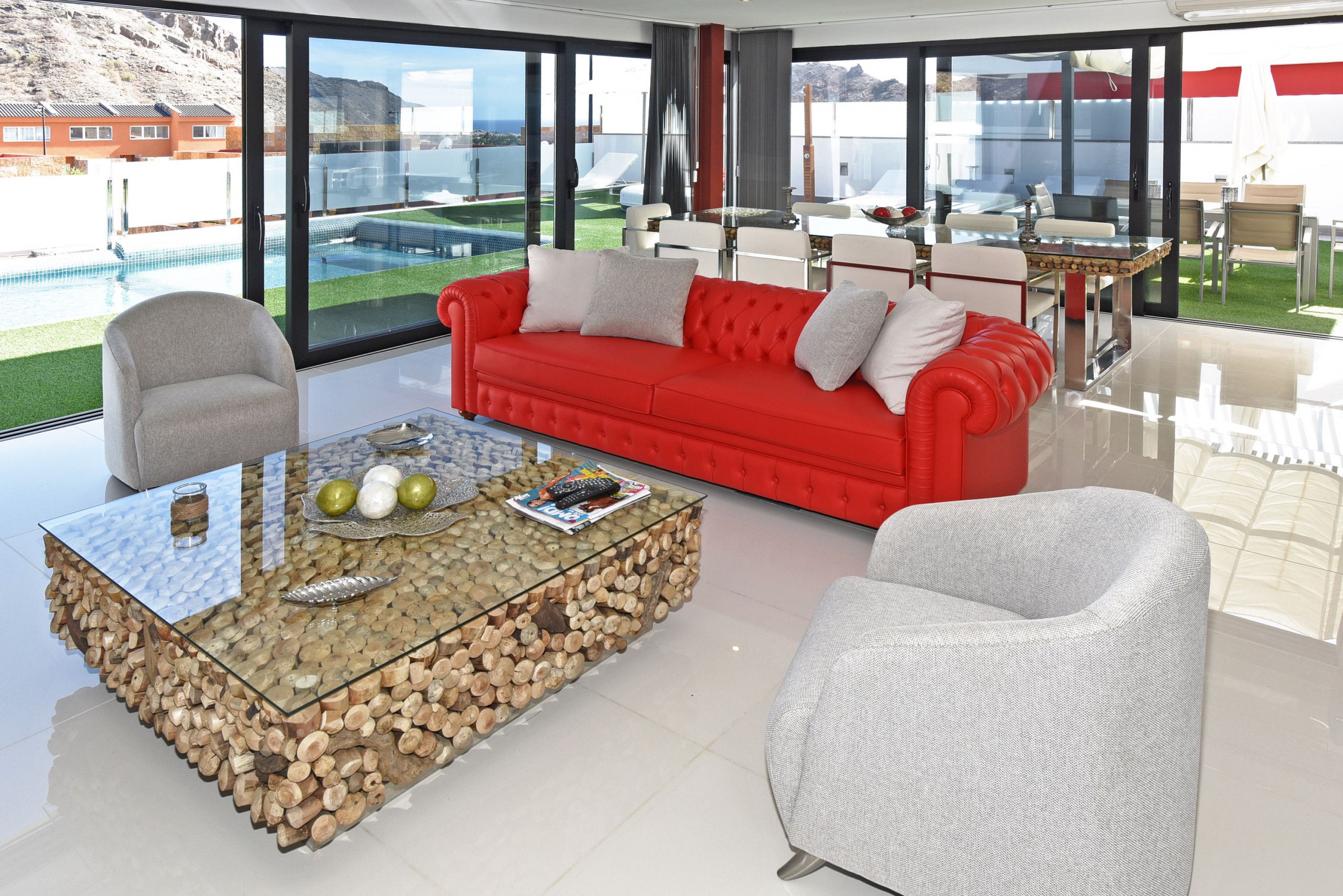 A modern living room with a glass coffee table, red sofa, and white armchairs.