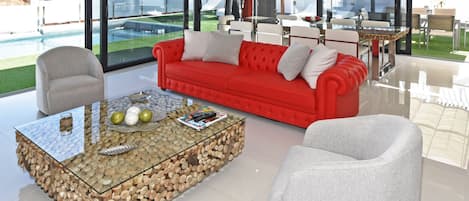 A modern living room with a glass coffee table, red sofa, and white armchairs.