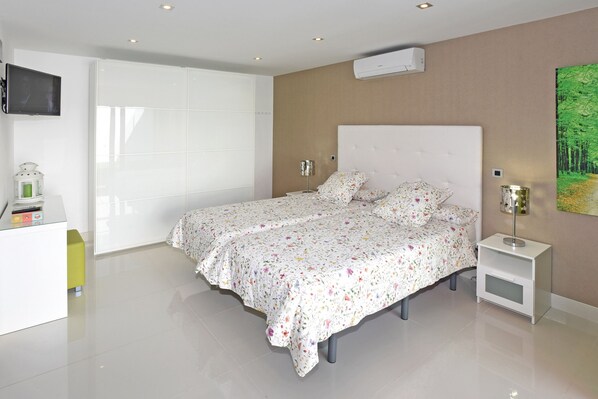 A modern bedroom with a large bed, a TV mounted on the wall, and a painting of a forest.