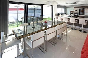 A modern kitchen with stainless steel appliances, a glass dining table with chairs, and a view of the outdoors. - Villa Morro del Guincho 29 (Mogán)