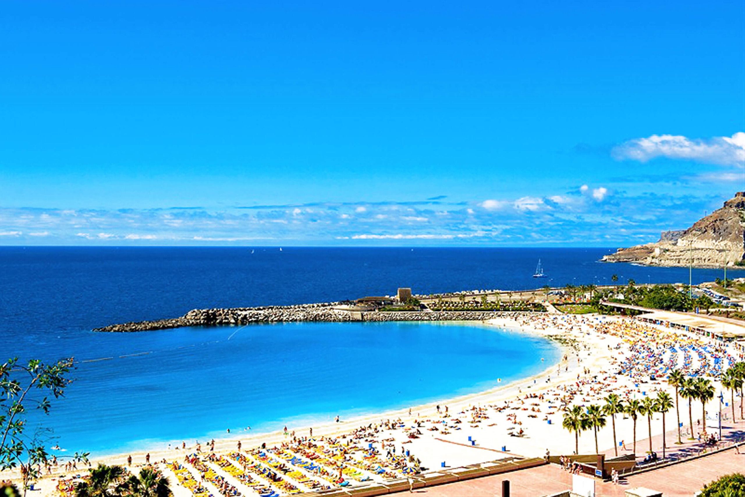 Ein Strand mit einer gewundenen Küstenlinie, einem Felsenmole und einem klaren, blauen Himmel.