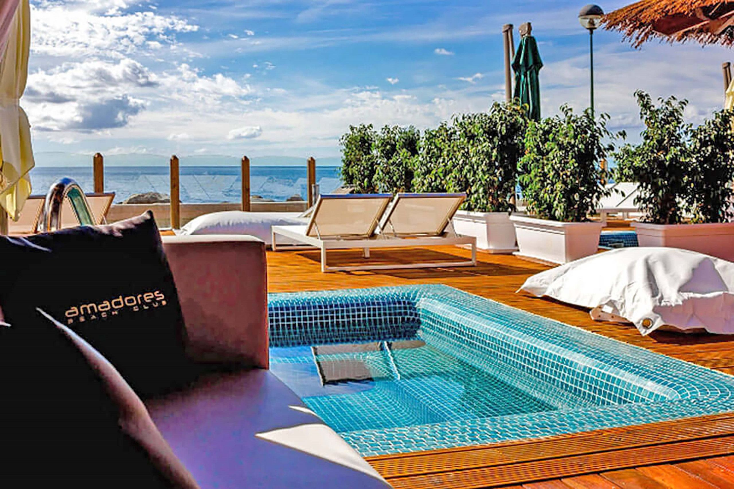 A pool area with lounge chairs, a small pool, and a view of the sea.