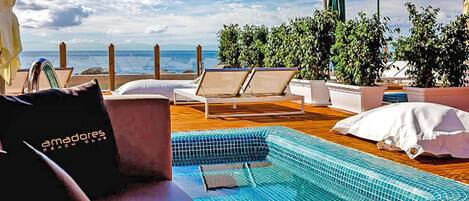 A pool area with lounge chairs, a small pool, and a view of the sea.
