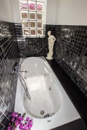 Bathroom features a bathtub, black mosaic tiles, and a window with a garden view.