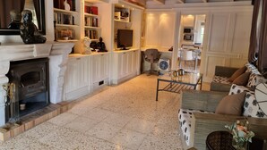 A spacious living room with a fireplace, a bookshelf, a dining area, and a kitchen in the background. - Stylish Finca Julia with 1000 sqm garden, priv. Pool, Air, BBQ, fireplace, terrace (Denia)