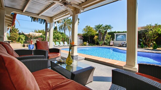 A covered outdoor seating area with wicker furniture, a glass-top table, and a view of a swimming pool. - Stylish Finca Julia with 1000 sqm garden, priv. Pool, Air, BBQ, fireplace, terrace (Denia)