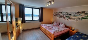 Une chambre à coucher comprenant un lit, une table de chevet, une commode, un radiateur, une fenêtre avec des rideaux et une fresque murale.