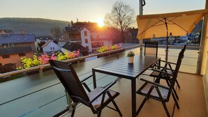 A balcony with a table and chairs, a potted plant, and a view of buildings and hills. - Apartment with garden and pool use (Rathmannsdorf)