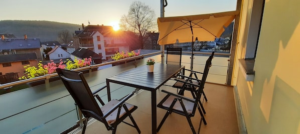 Un balcon avec une table et des chaises, un pot de fleurs et une vue sur des bâtiments et des collines.