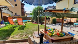 A backyard with a wooden play area, two orange lawn chairs, a wooden deck, and a covered seating area with a table and chairs. - Apartment with garden and pool use (Rathmannsdorf)