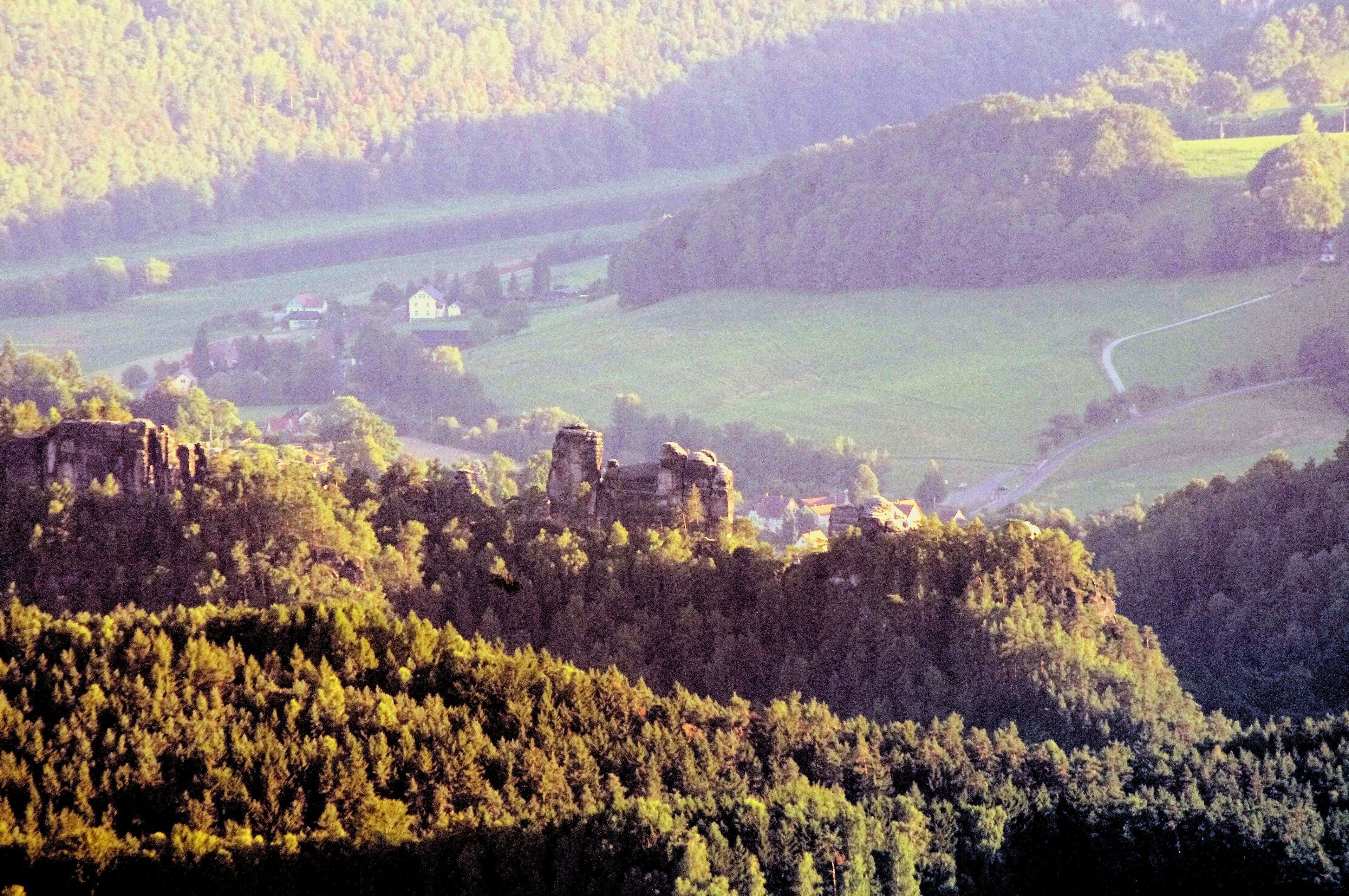 Ein historisches Steingebäude auf einem Hügel mit Blick auf eine ländliche Landschaft, darunter Felder und verstreute Gebäude.