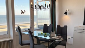 Un coin repas avec une table en verre, des chaises, un lustre, une vue sur la mer et un buffet blanc.