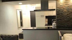 Un salon moderne avec un canapé, une table basse et un lit. On aperçoit, au fond, un coin cuisine avec un réfrigérateur et une cuisinière.