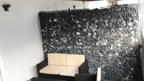 Un espace extérieur aménagé avec un canapé et des fauteuils, une petite table et un mur en pierre en arrière-plan.