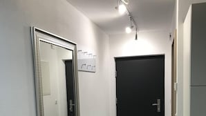 Un couloir avec un grand miroir, une porte noire et un petit pouf.