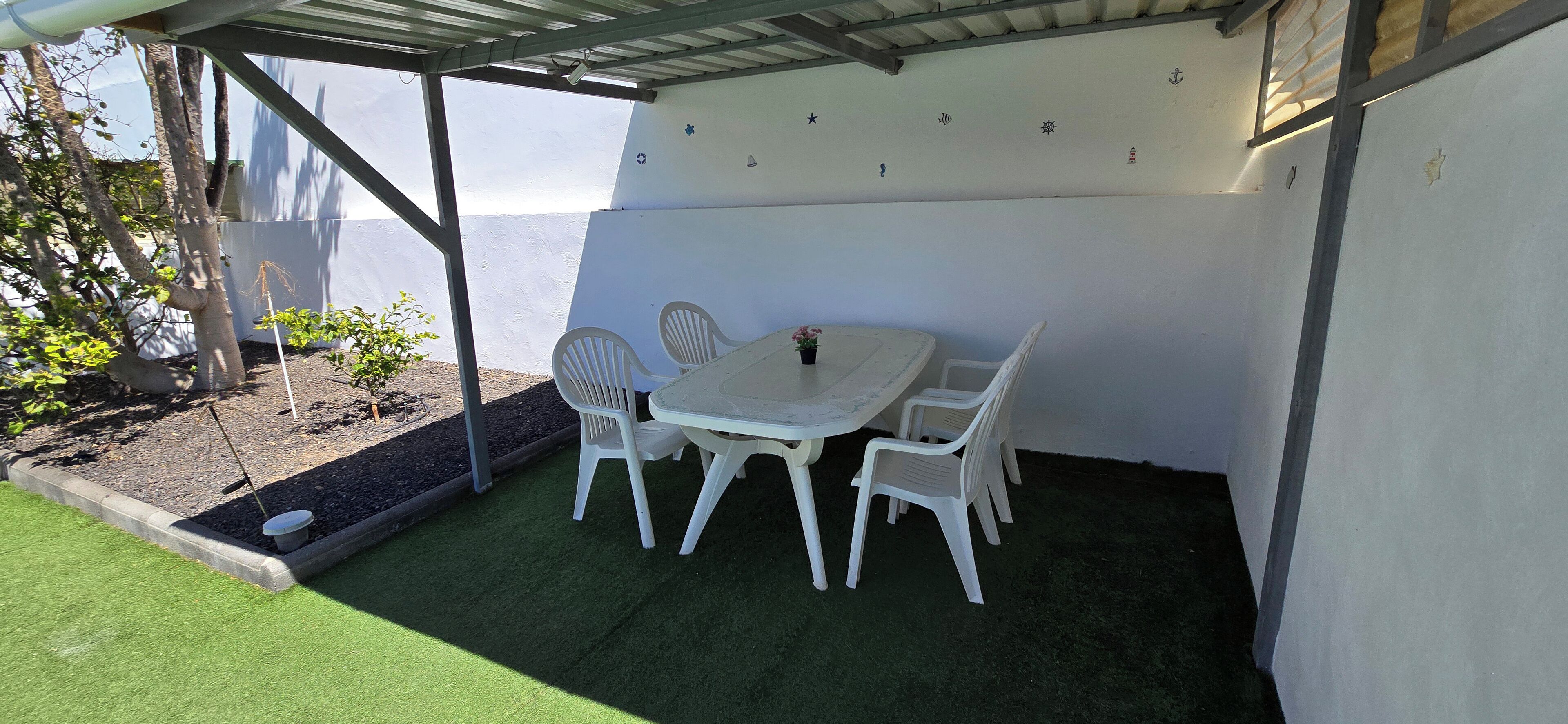 En overdækket terrasse med et bord og stole, et lille haveområde og havudsigt.
