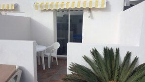 Eine kleine Terrasse mit weißem Tisch und Stühlen, einer Glasschiebetür und einem gelb gestreiften Markisenvorzelt.