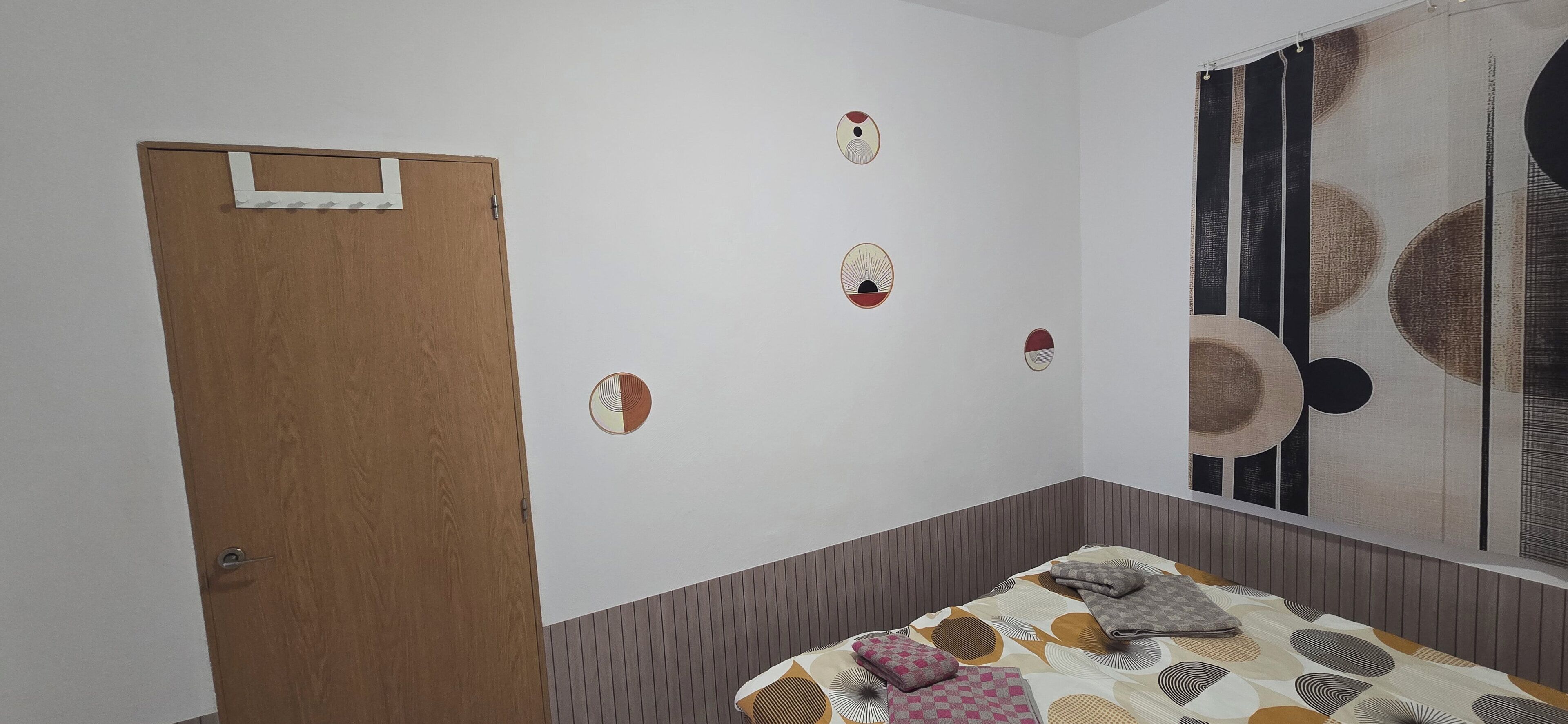 A bedroom with a wooden door, a bed with patterned bedding, and a large abstract wall art piece.