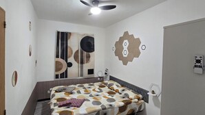 Ein Schlafzimmer mit einem Bett, einem Deckenventilator, einer Wandleuchte und einer Tür.