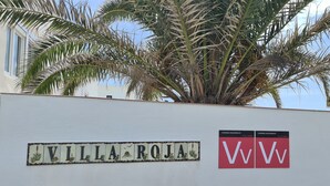 Schild für 'Villa Roja' mit dekorativem Rahmen und dem Logo 'WW' an einer weißen Wand.