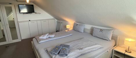 A bedroom with a bed, a TV mounted on the wall, a bedside table with a lamp, and a wardrobe.