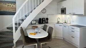 Eine moderne Küche mit weißen Schränken, einem Esstisch mit Stühlen, einer Treppe und einem Wandbild mit Strandmotiv.