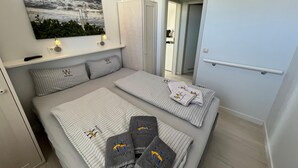 Ein Hotelzimmer mit einem Bett, einem Meeresbild, einem Schrank und einem durch eine offene Tür einsehbaren Badezimmer.