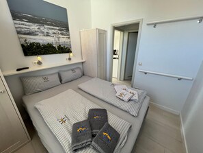A hotel room with a bed, a painting of the sea, a wardrobe, and a bathroom visible through an open door. - Bernstein - modern vacation apartment in the rose garden (Wangerooge)