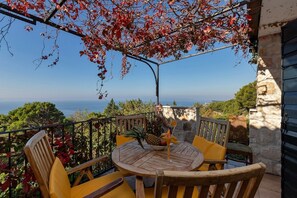 Une table en bois, entourée de chaises, sur un balcon donnant sur la mer.