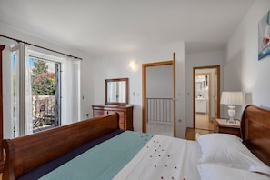 Une chambre à coucher avec un lit en bois, une commode, un miroir et un balcon donnant sur des arbres et une clôture.