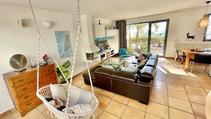 Un salon moderne avec un fauteuil suspendu, un canapé, un coin repas et une vue à travers la porte vitrée.