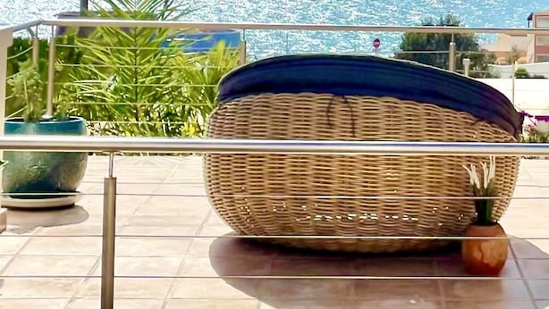 Une chaise en osier avec un coussin foncé, placée sur un balcon donnant sur la mer.