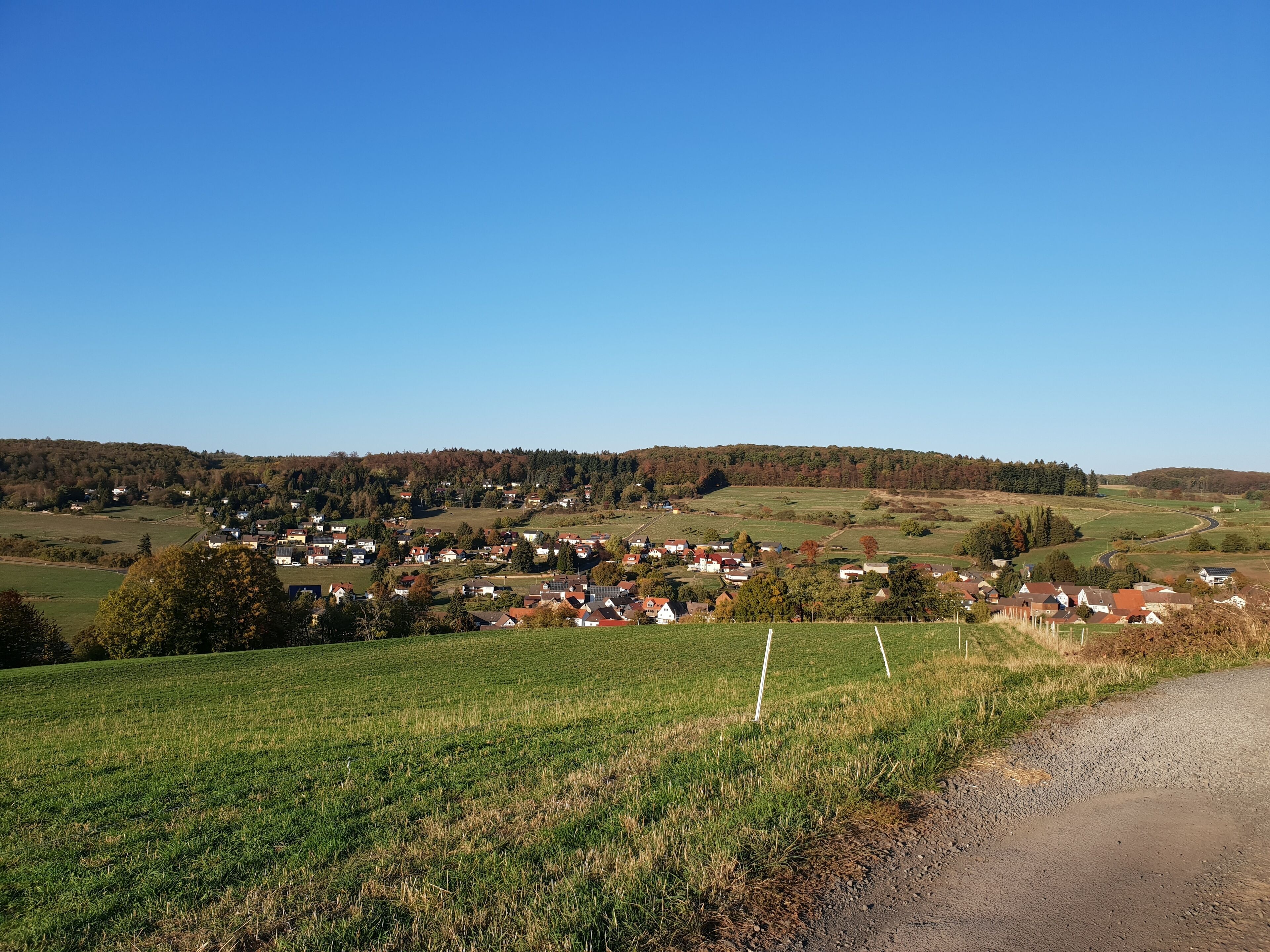 Paesaggio rurale con un piccolo villaggio, campi verdi e una strada tortuosa.